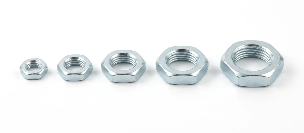 Five zinc plated thin hex nuts in a row on white, visibly low compared with a standard nut